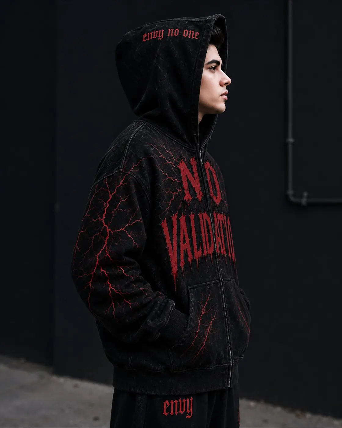 Model in the ENVIED No Validation washed black zip hoodie with red lightning print against a dark wall